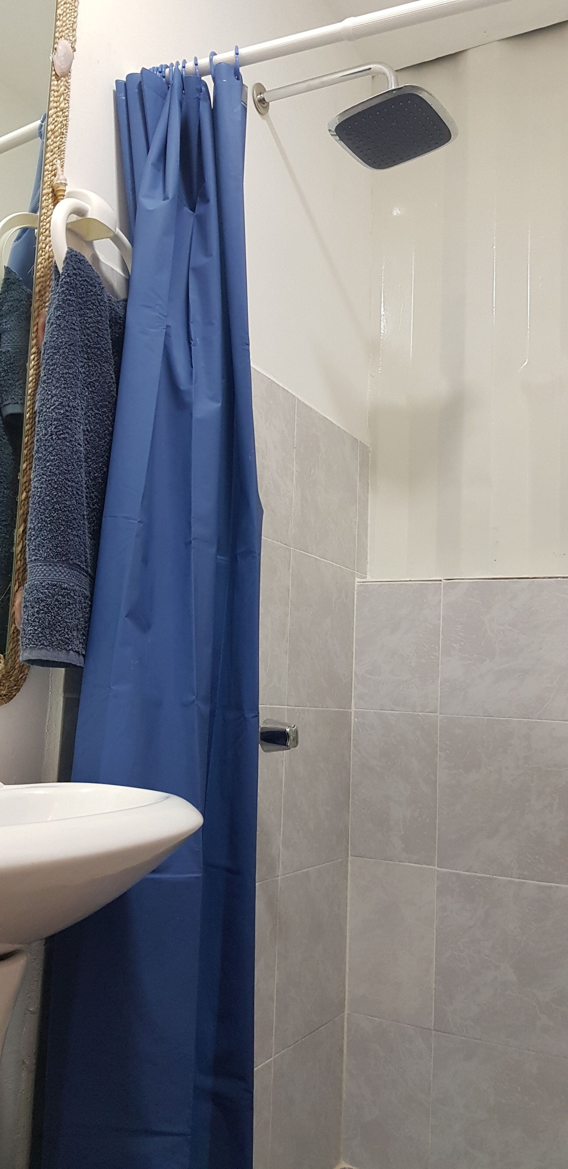 Un baño con un lavamanos blanco, una ducha con cortina azul y un perchero con una toalla azul.