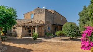 A rustic stone building with a tiled roof, surrounded by greenery and a gravel path.