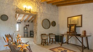 A rustic room with exposed wooden beams, a traditional wooden table, two chairs, a patterned rug, and a wall-mounted map.
