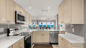 Une cuisine moderne avec des armoires de couleur beige, des appareils en acier inoxydable et une vue sur l’océan grâce à de grandes fenêtres.