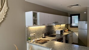 Una cocina moderna con gabinetes blancos, encimeras de granito, microondas integrado y refrigerador de acero inoxidable.