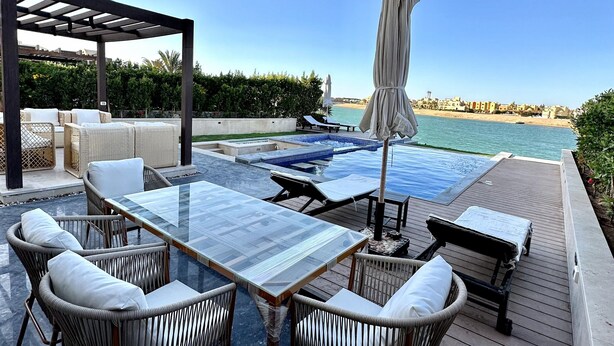 Zona junto a la piscina con mobiliario de mimbre, una mesa de vidrio y vistas a la playa.