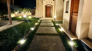 Un edificio moderno con una entrada central, un camino bien iluminado y un pequeño jardín.