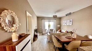 Una sala de estar moderna con una mesa de comedor de madera, sofás color beige y un espejo grande con un marco decorativo.