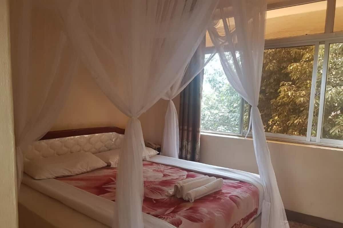 A bed with a canopy, a window with a view of trees, and a bedside table.
