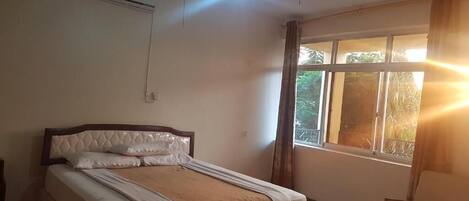 Quarto com cama, ar condicionado, janela com cortinas e uma cadeira.