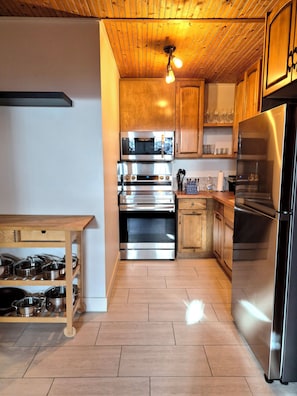 A modern kitchen with stainless steel appliances, wooden cabinets, and a wooden ceiling.