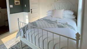 Ett sovrum med ett träpanelat tak, vita väggar, en vit säng med en metallram och en grå, mönstrad matta.