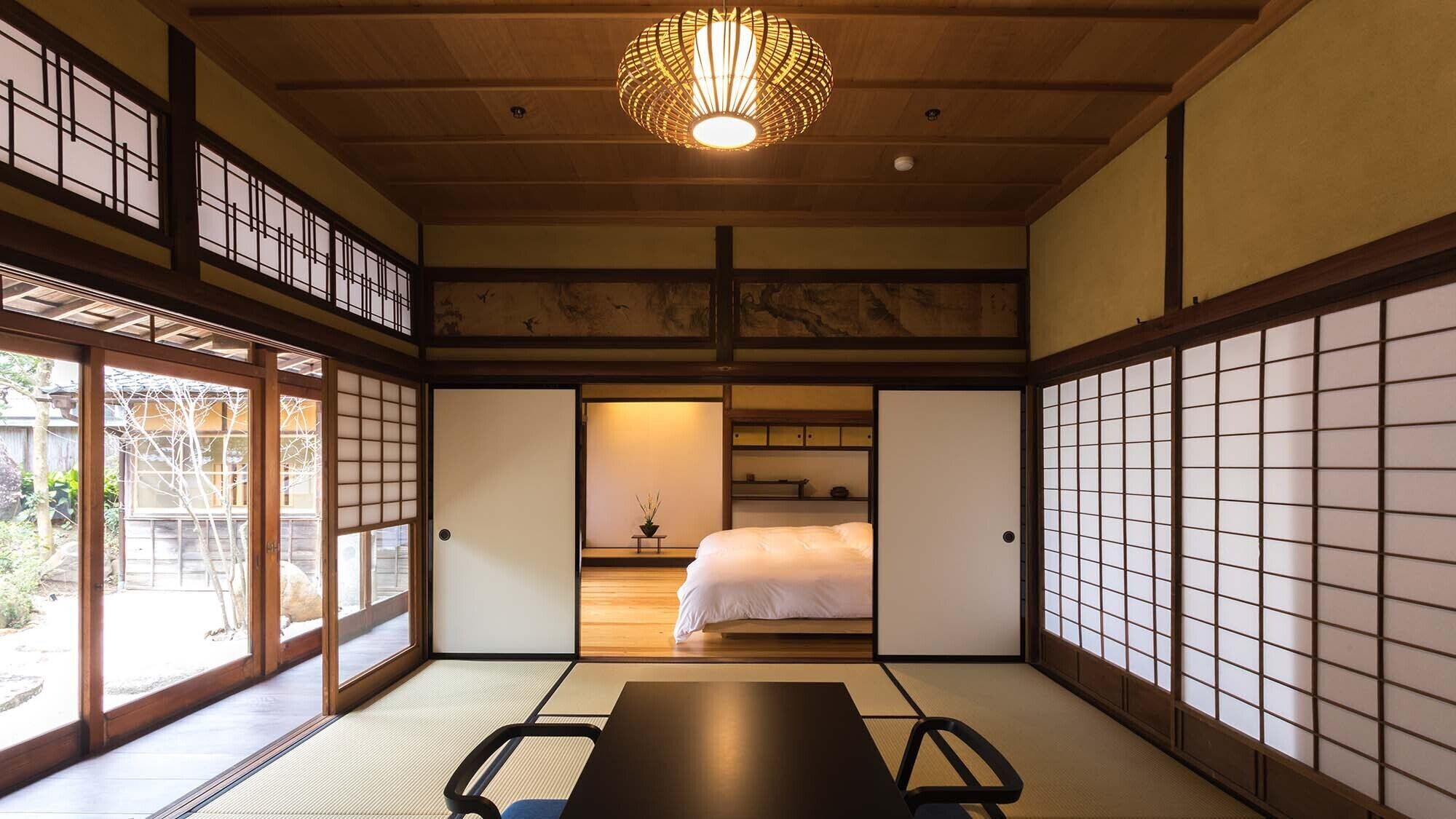 Een traditionele Japanse kamer met tatami vloeren, een bed, een tafel en een hangende lamp.
