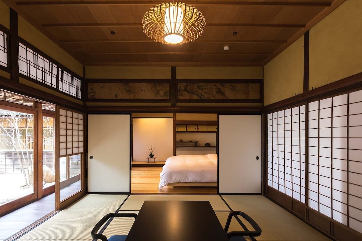 Een traditionele Japanse kamer met tatami vloeren, een bed, een tafel en een hangende lamp.