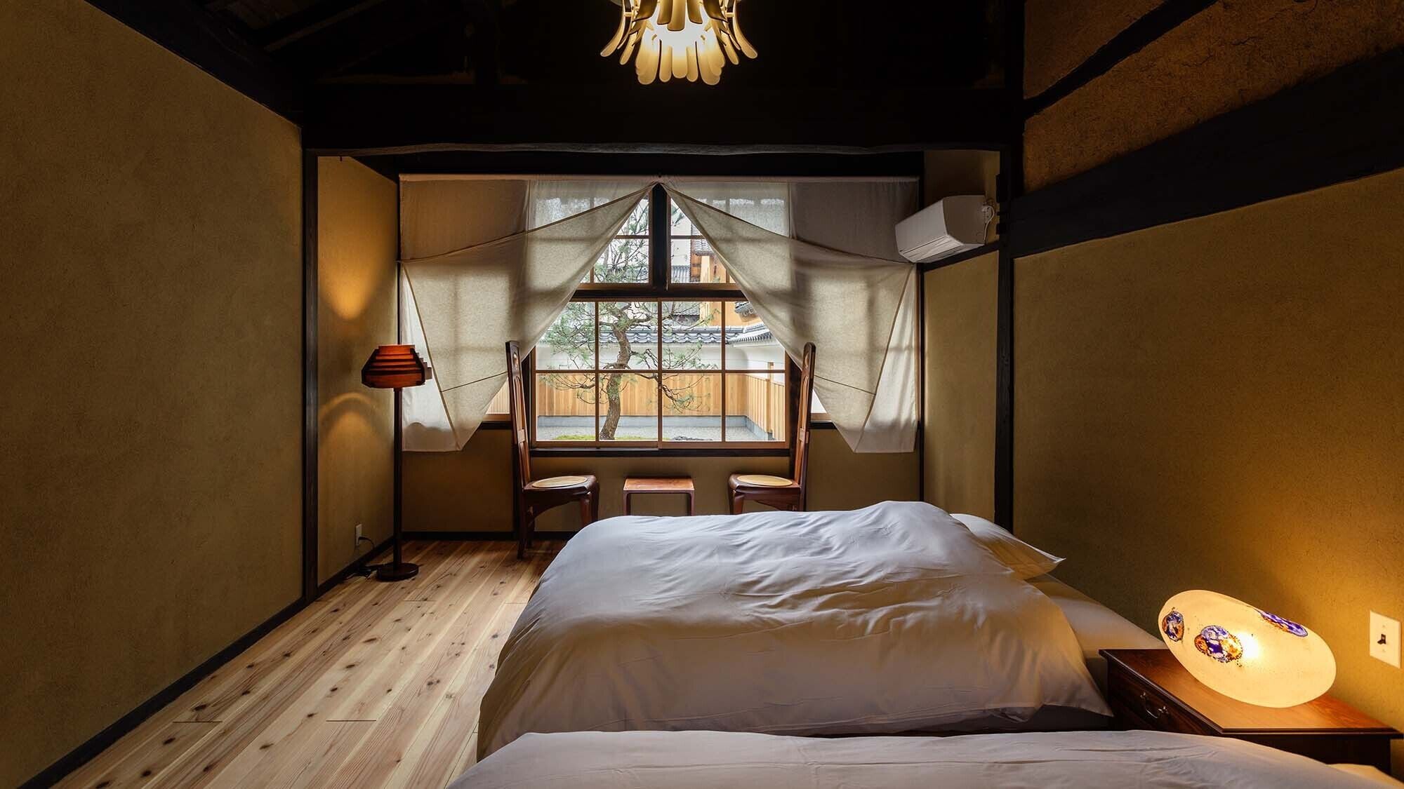 Een kamer met een bed, een raam met uitzicht op een traditioneel gebouw, een lamp en een plafondarmatuur.