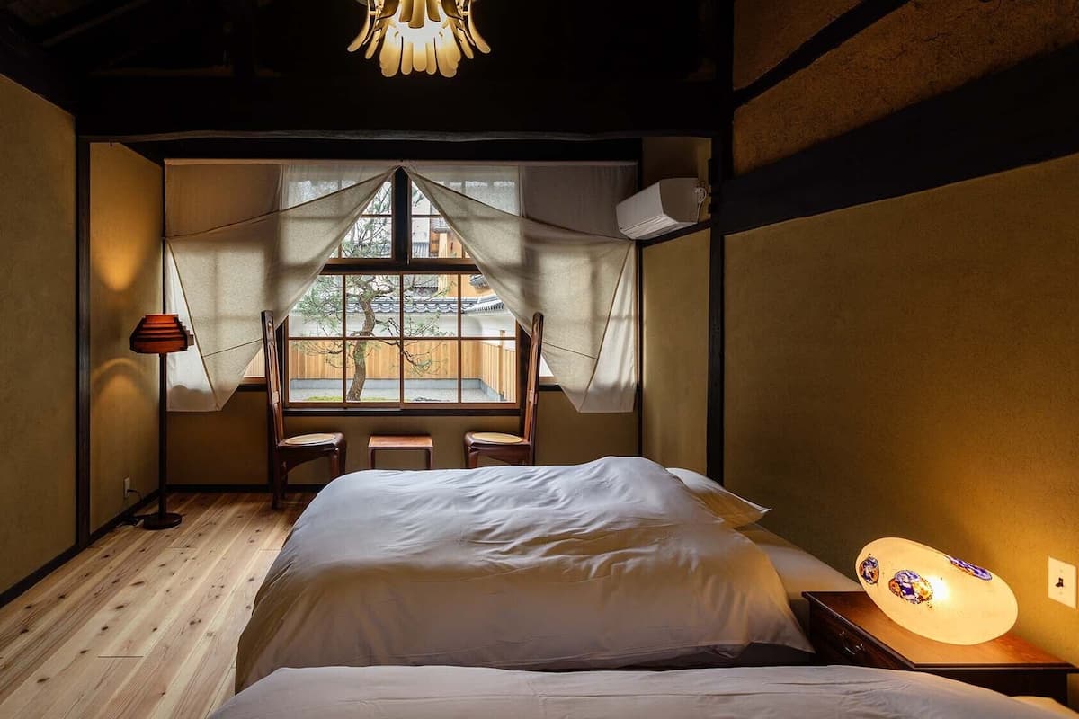 Een kamer met een bed, een raam met uitzicht op een traditioneel gebouw, een lamp en een plafondarmatuur.