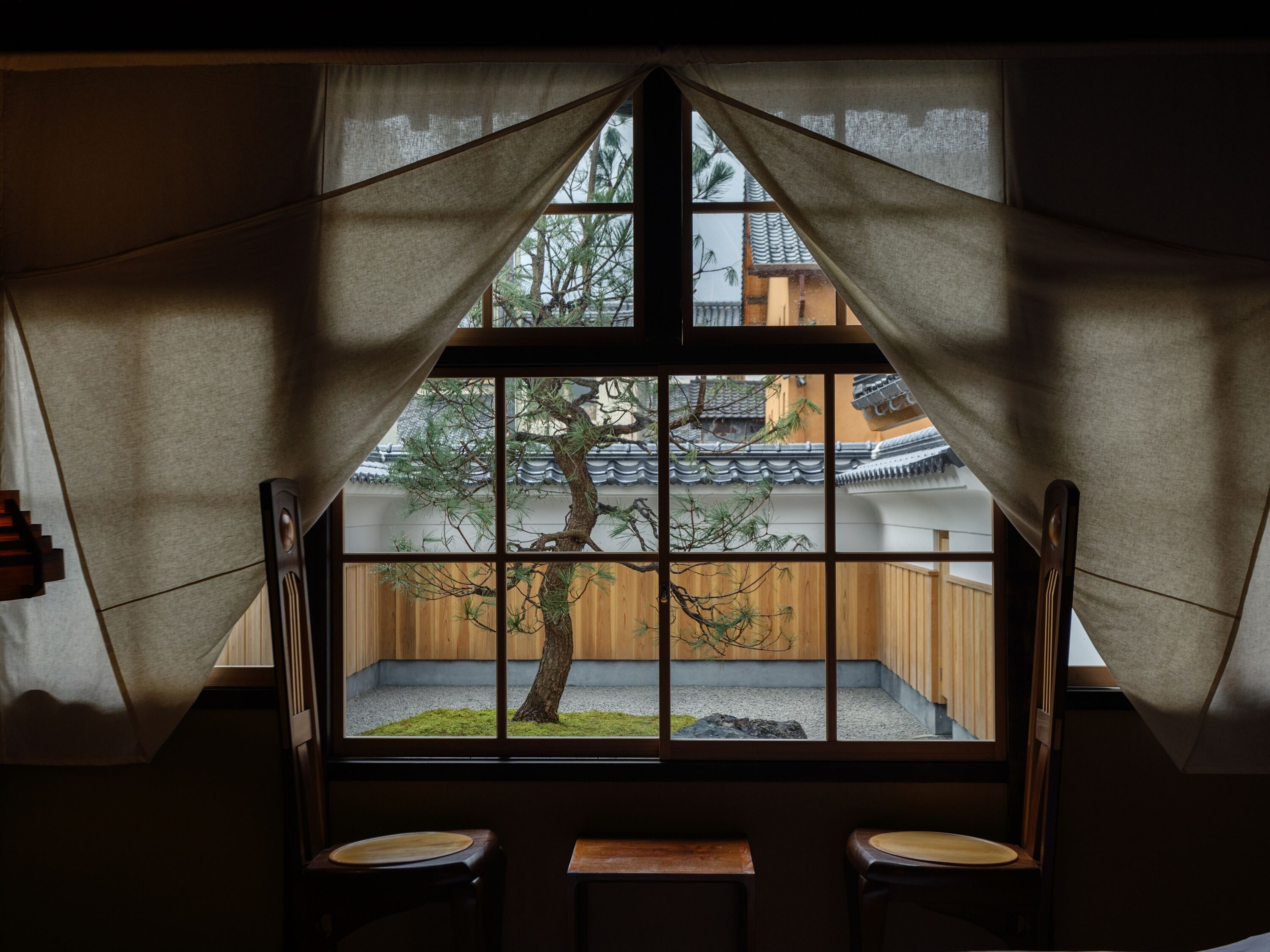 A room with a large window framed by curtains, a wooden desk, and a chair.