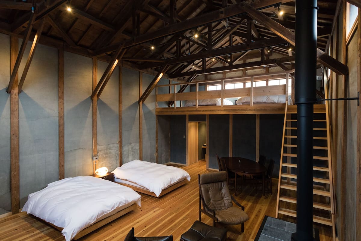 Een rustieke kamer met twee bedden, een houten tafel en een open haard.