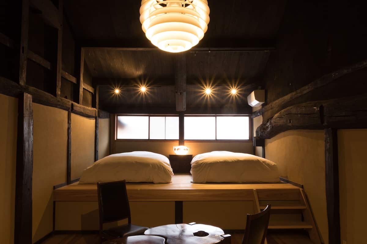 Een kamer met een bed, twee stoelen, een tafeltje en een hanglamp.