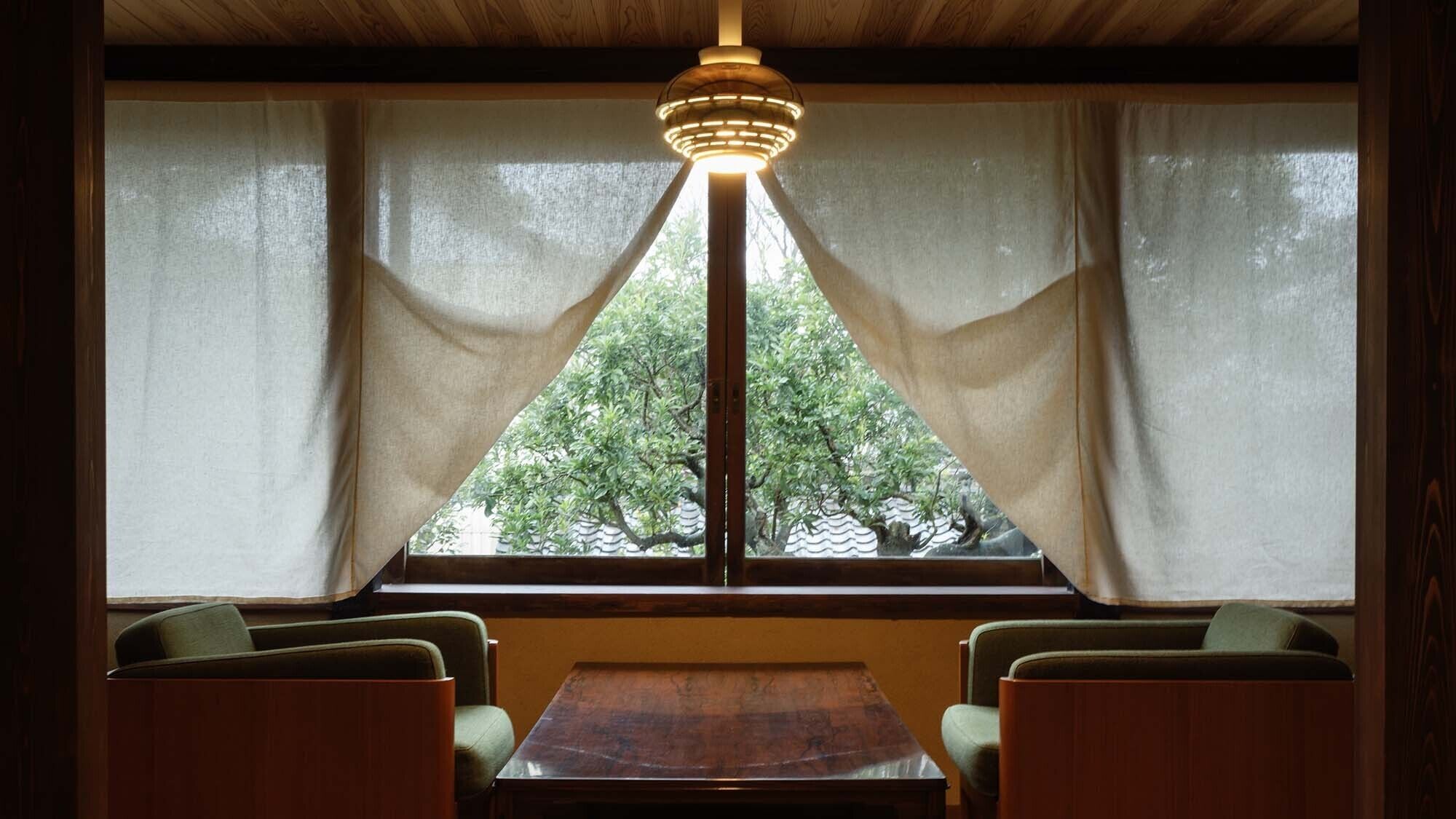 Een kamer met houten plafond, een tafel, twee stoelen en een raam met gordijnen.