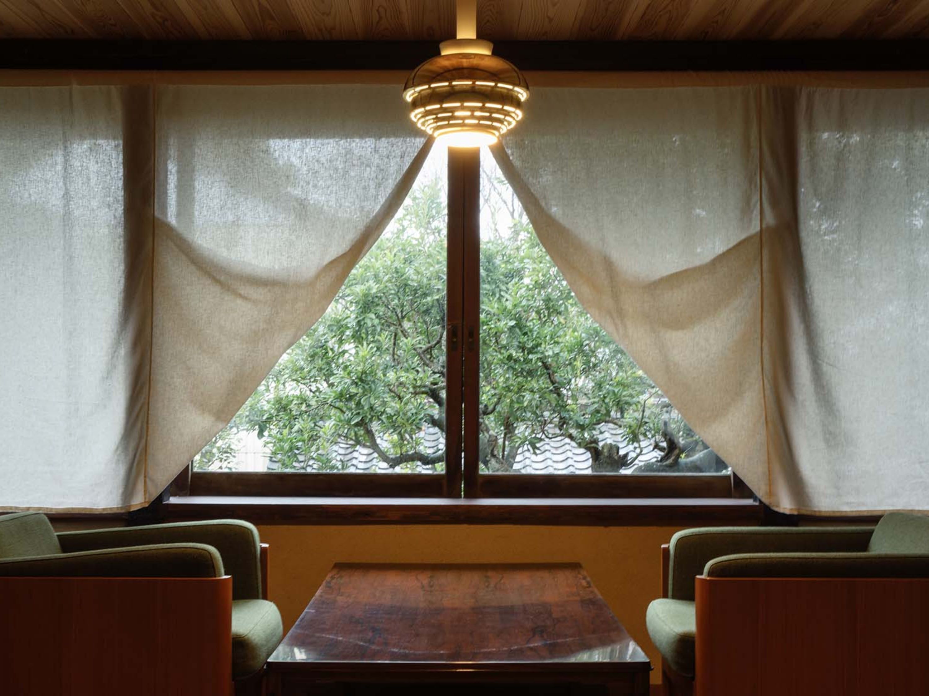 A room with a wooden ceiling, a table, two chairs, and a window with curtains.