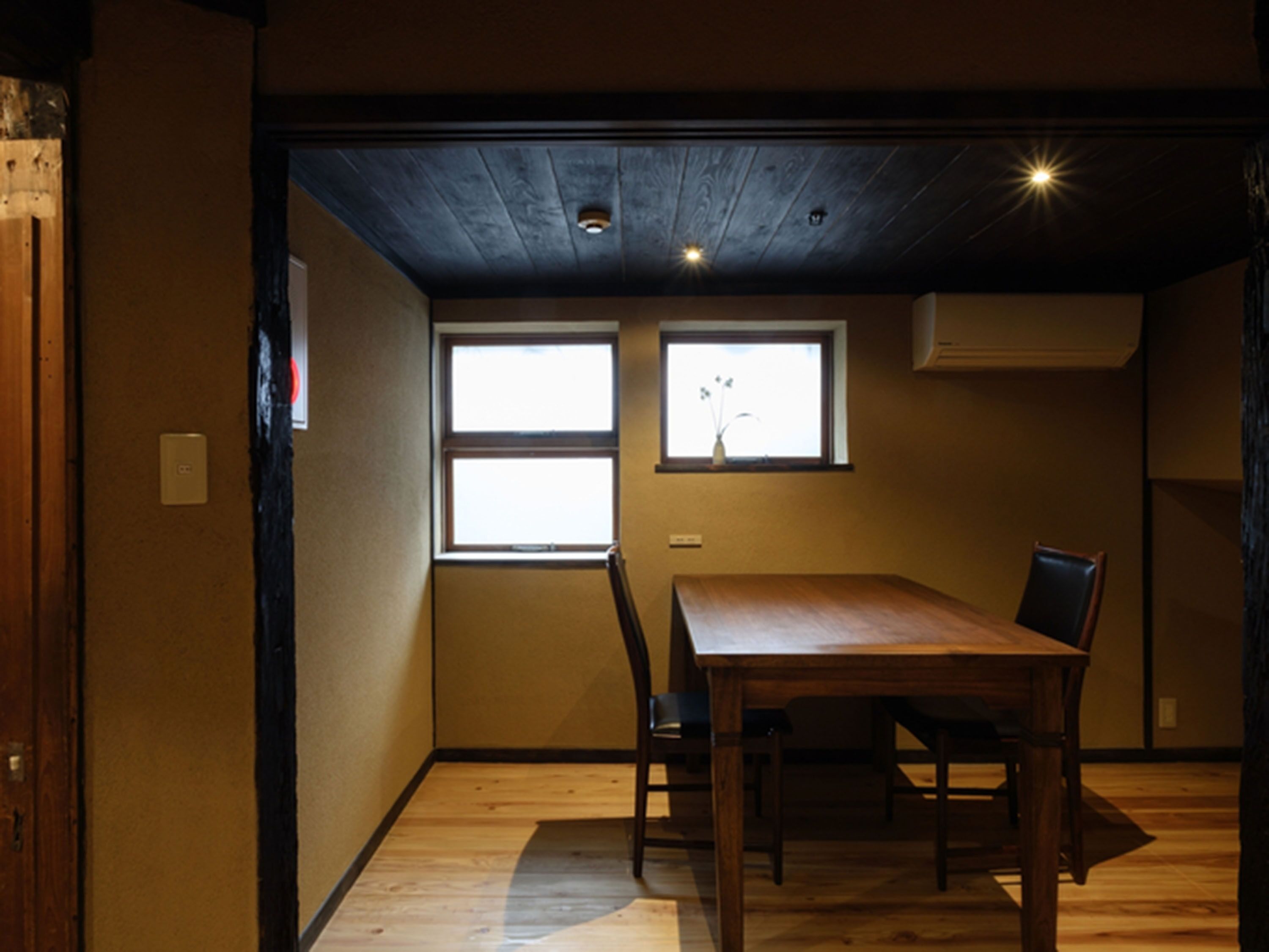 A room with a wooden dining table, two chairs, and two windows with blinds.