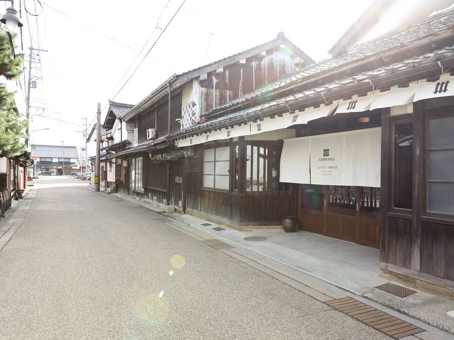 Een traditionele Japanse straat met houten gebouwen, een heldere lucht en een bord met 'Nipponia' aan de rechterkant.
