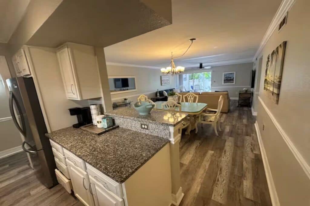 A kitchen with granite countertops, white cabinetry, a dining area with a table and chairs, and a chandelier.