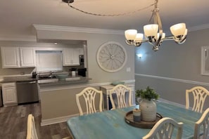 A dining area with a blue table, white chairs, a chandelier, and a clock on the wall. - Paradise Escape 5 min to Siesta Key Beach First Floor sleeps 6 refreshed '26 (Sarasota)
