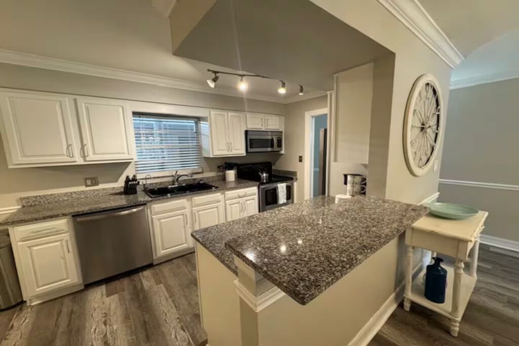 A kitchen with white cabinets, a granite countertop, stainless steel appliances, and a clock on the wall.