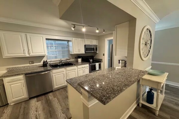 A kitchen with white cabinets, a granite countertop, stainless steel appliances, and a clock on the wall. - Paradise Escape 5 min to Siesta Key Beach First Floor sleeps 6 refreshed '26 (Sarasota)