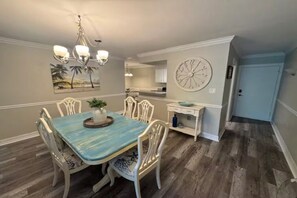 A dining area with a table, chairs, a chandelier, a clock, and a kitchen in the background. - Paradise Escape 5 min to Siesta Key Beach First Floor sleeps 6 refreshed '26 (Sarasota)