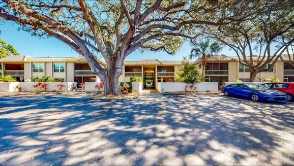 A motel with a central tree, a parking lot, and two cars parked. - Paradise Escape 5 min to Siesta Key Beach First Floor sleeps 6 refreshed '26 (Sarasota)