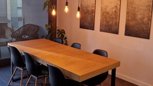 Una sala de reuniones moderna con una larga mesa de madera, sillas negras, bombillas colgantes y arte abstracto en la pared.