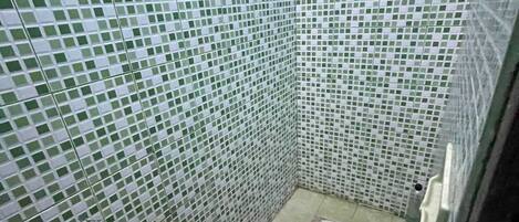 A small, tiled bathroom with a squat toilet, a red bucket, and a red scoop.