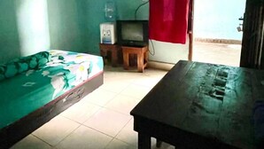 Una habitación pequeña con una cama, una mesa, un televisor y una ventana con cortina roja.