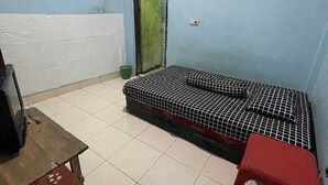 Una habitación pequeña y escasamente amoblada con una cama individual, una mesita y un taburete rojo.