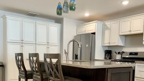 Une cuisine moderne avec des meubles blancs, un îlot central doté de tabourets, des appareils en acier inoxydable et un éclairage suspendu.