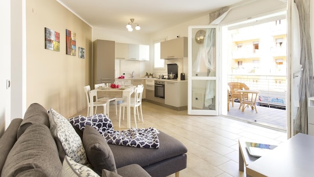 Um apartamento moderno com sala de estar, espaço para refeições, cozinha compacta e varanda com mobiliário de vime.