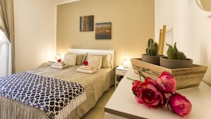 Quarto de hotel bem arrumado, com cama, mesas de cabeceira, um criado-mudo e uma pequena escrivaninha com um vaso de flores.