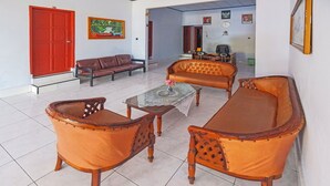 Un salon avec une porte rouge, un canapé marron, une table basse en verre et des fauteuils orange.