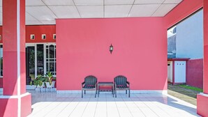 Un espace extérieur abrité, avec deux chaises et une table, un mur rouge et un sol carrelé.