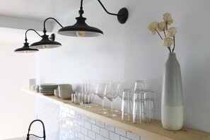 A kitchen counter with a vase of flowers, a variety of glassware, and hanging pendant lights.