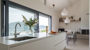 Cozinha moderna com uma ilha grande, pia embutida e vista para o exterior. Há luminárias pendentes e uma pequena planta na prateleira.