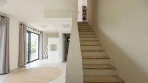Um interior moderno com escada que leva a um mezanino, uma janela grande e um tapete circular.