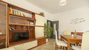 Ein Wohnzimmer mit einer Holztrennwandschrank, einem Fernseher, einem Esstisch mit Stühlen und einer Zimmerpflanze.