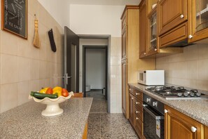 Una cocina con encimera de granito, microondas, estufa, armarios de madera y un cuenco de fruta sobre la encimera.