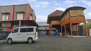 Een gebouw met een rode en grijze gevel, een overdekte houten constructie en een witte bestelwagen er voor.