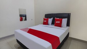 Een net opgemaakt bed met een wit-rode sprei, een zwart hoofdeinde en twee kussens met de tekst 'OYO'.