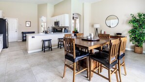 Una cocina moderna con armarios blancos, una isla central y un comedor con sillas y mesa de madera.