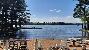 A lakeside view with a sandy beach, lounge chairs, and a picnic table.