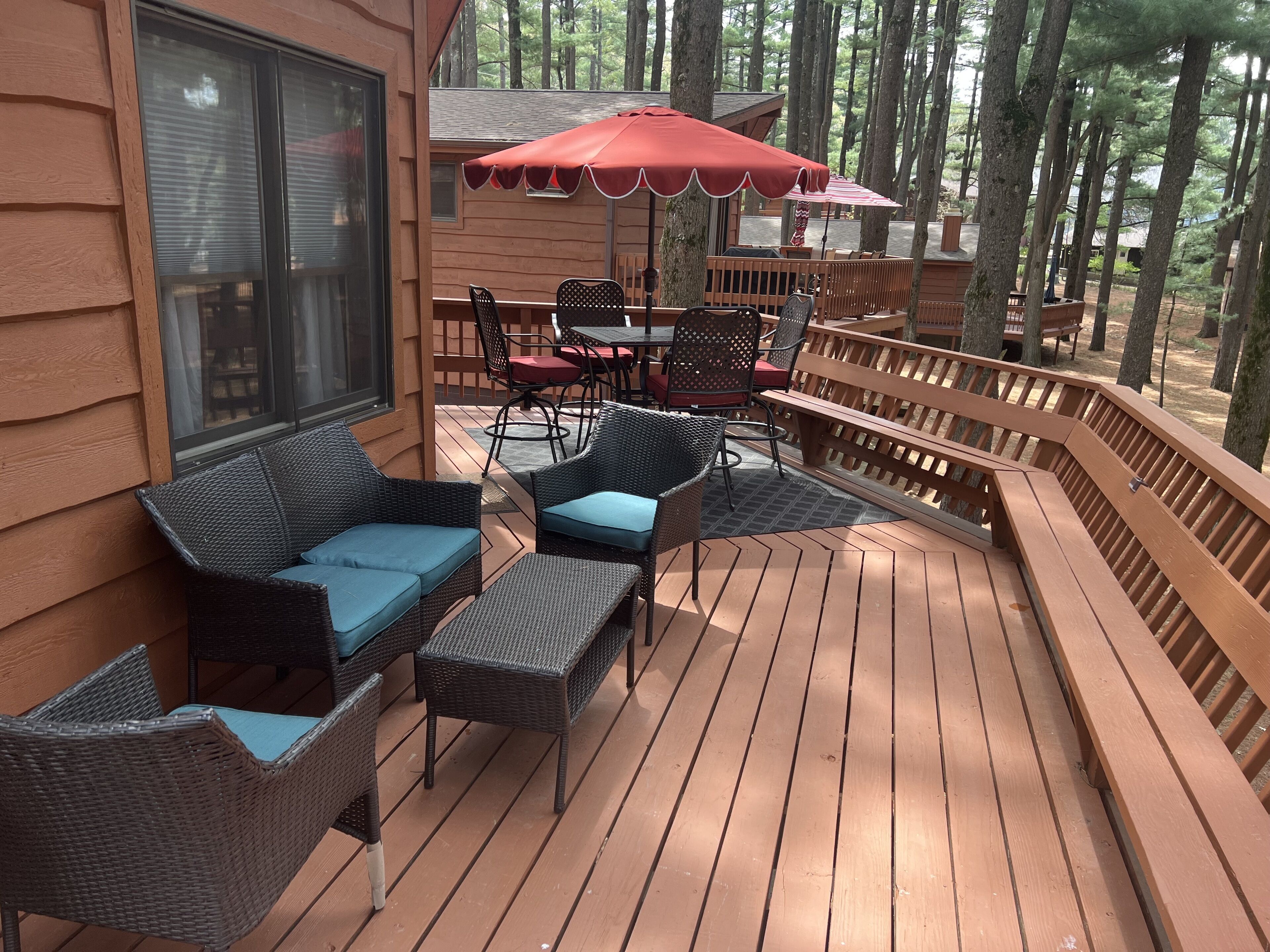 Una terraza de madera con mobiliario de mimbre y un paraguas rojo.