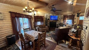 A cozy cabin interior with a dining table, chairs, a sofa, a fireplace, a television, and a ceiling fan. - Lake view 2 bedroom House on Lake Delton Resort. Beaches. Pool. Playground! (Lake Delton)