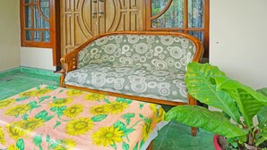 A room with a wooden sofa, a patterned cushion, a floral table runner, and a potted plant. - SPOT ON 91527 As-sakinah Homestay Syariah (Surabaya)